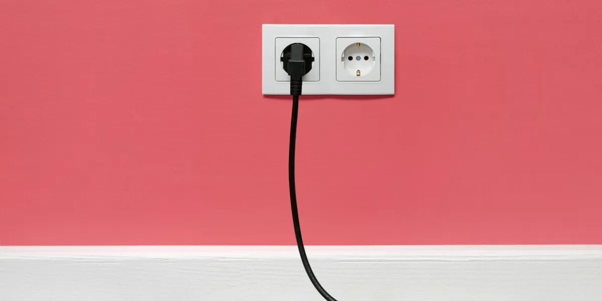 white double outlet installed on pink wall with inserted black electrical plug, front view