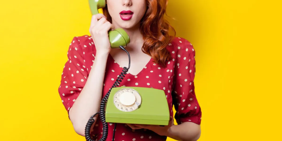 surprised redhead girl in red polka dot dress with green dial phone on yellow background