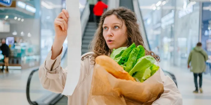 rising food prices surprised woman looking into a paper check at the mall, holding a paper bag with fresh herbs and a baguette