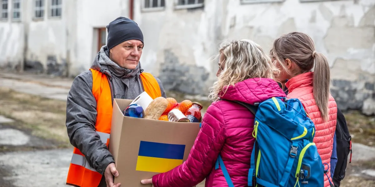 volunteer in orange west gives a box of food donation to fleeing refugees from ukraine