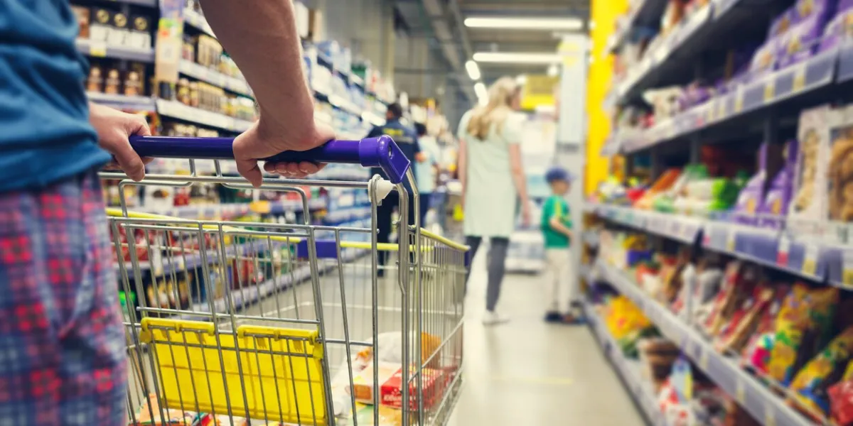 man with a basket walks in a supermarket hand and part of the basket in focus, blurred background
