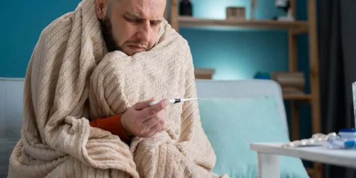 man wrapping in plaid holding at digital thermometer for measuring body temperature sick male with cold and fever copy space