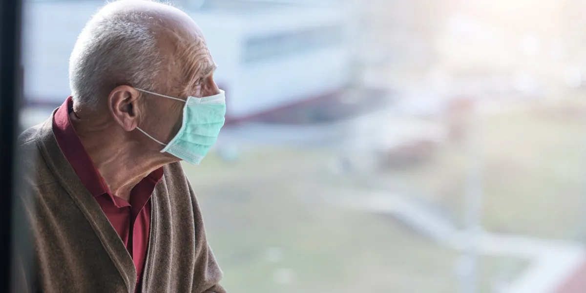 aged pensioner man with gray hair wearing medical facemask looking through window health care concept