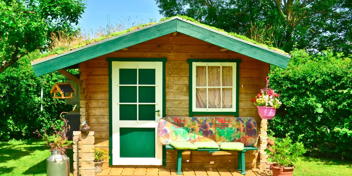 a light green and wooden small shed, gardenhouse, with a bench some tools around it