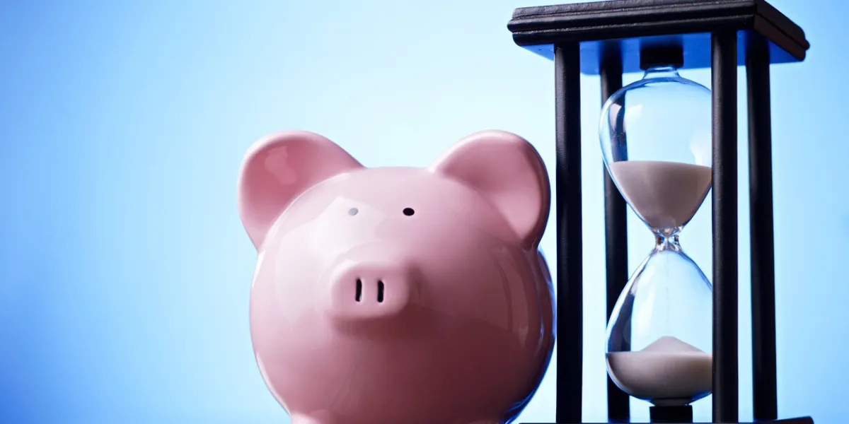 close-up of a pink porcelain piggy bank with a vintage hourglass behind, concept of saving money and passing time