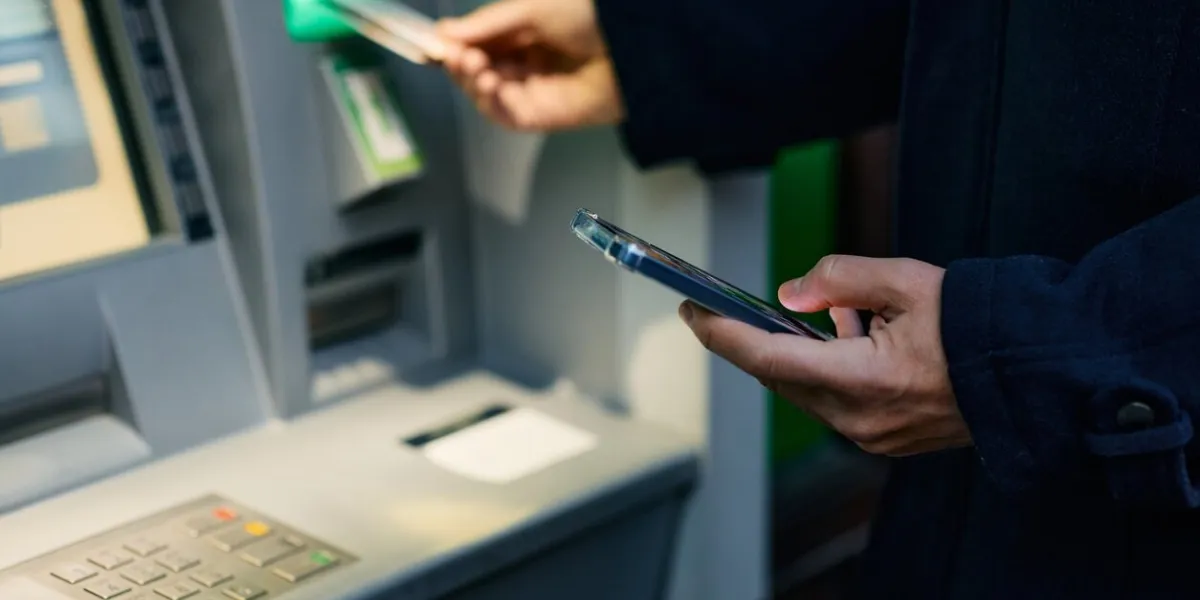 close up of using cell phone while inserting credit card in atm machine