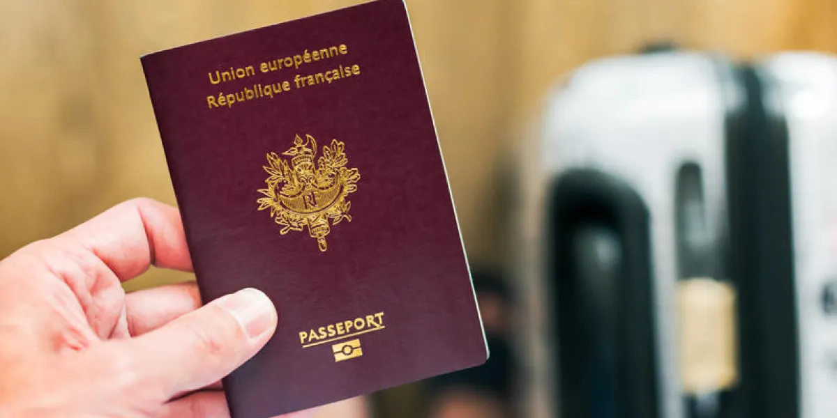 hand holding a french - european passport with luggage in the background