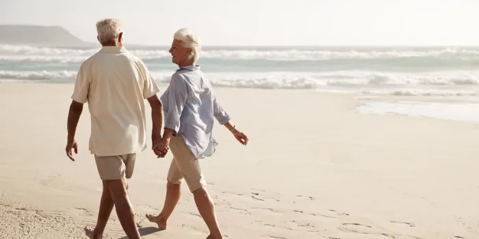 rear view of senior couple walking along beach hand in hand