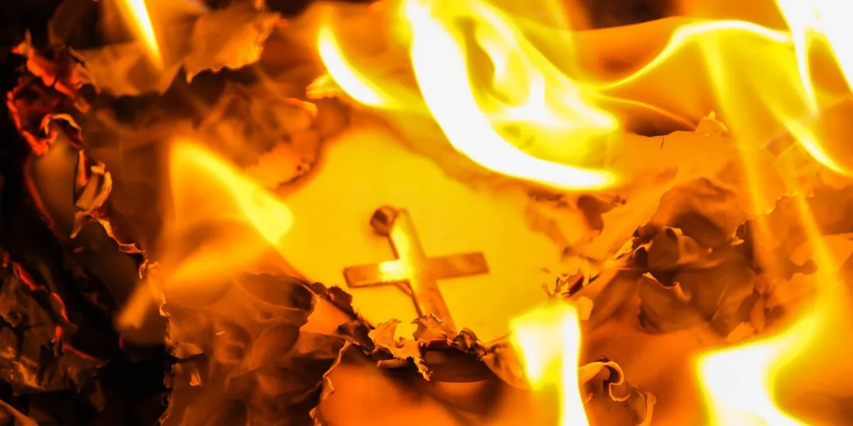 flames on a burning silver cross blazing in the night close up burning paper with silver cross placed in center on black background