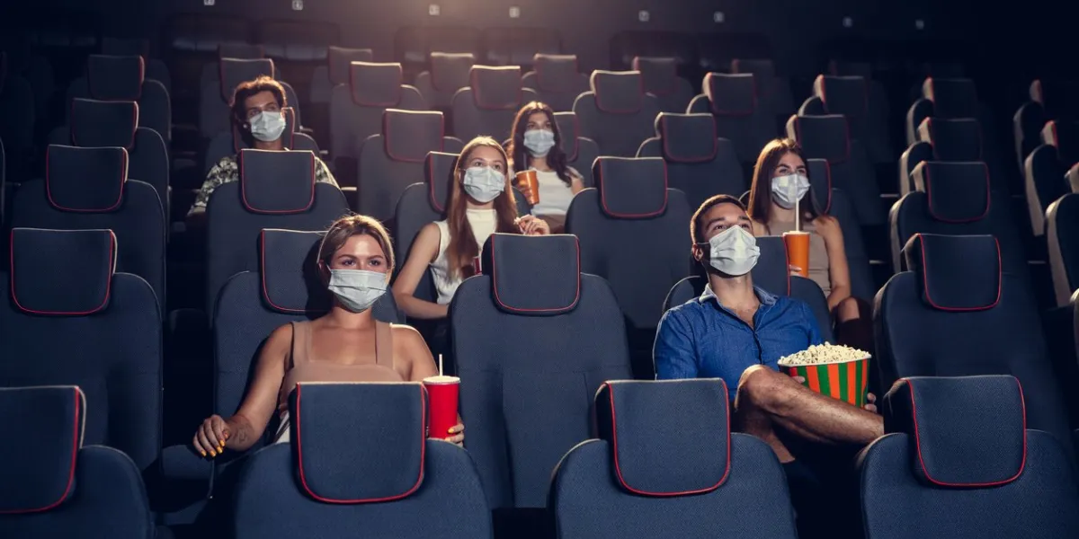 cinema, movie theatre during quarantine coronavirus pandemic safety rules, social distance during movie watching men and women wearing protective face mask sitting in a rows of auditorium, eating popcorn