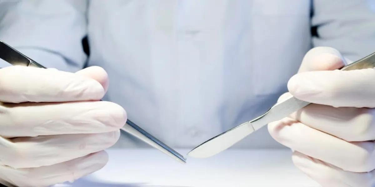 mains dans des gants en caoutchouc médicaux tenant des pinces métalliques et un scalpel