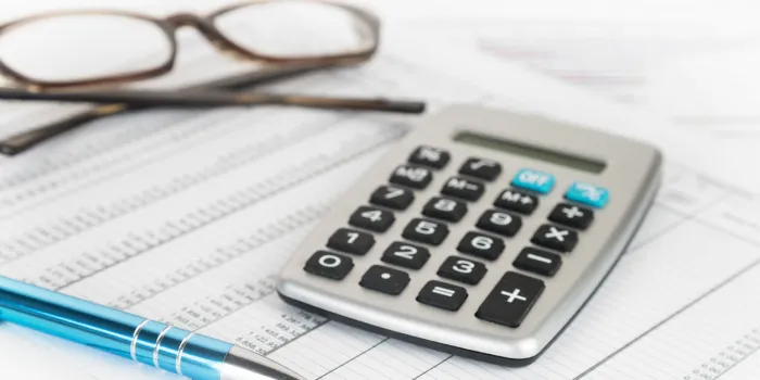 calculator, pen and glasses on a printed financial report with number tables, business concept for finance, economy and taxes, selected focus, narrow depth of field