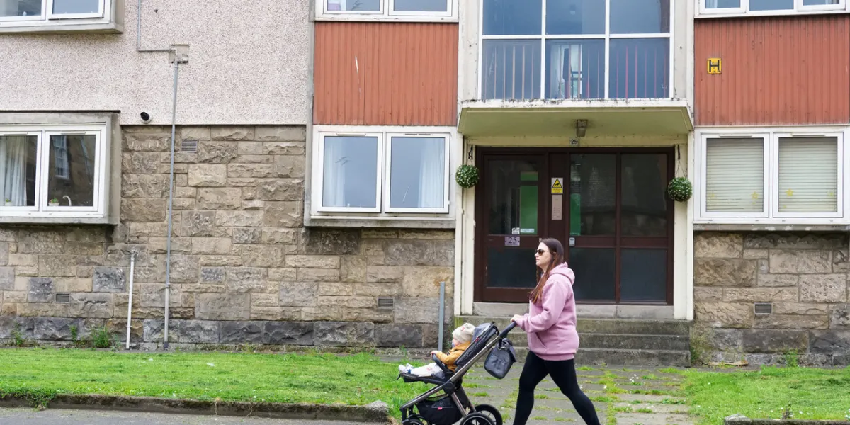 paisley, scotland, uk, august 7th 2022 mother walking past council flats in poor housing estate with many social welfare problems uk