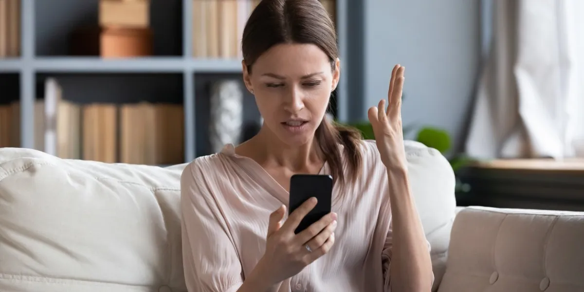 confused angry woman having problem with phone, sitting on couch at home, unhappy young female looking at screen, dissatisfied by discharged or broken smartphone, reading bad news in message