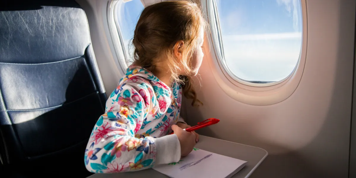 child drawing picture with crayons in airplane little girl occupied while flying in aircraft travel with family and kids blue sky and sun outside the window