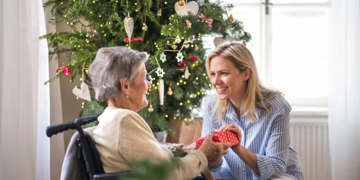 a health visitor and a senior woman in wheelchair with a present at home at christmas time