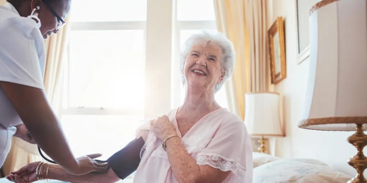 female doctor measuring blood pressure of senior woman elderly woman sitting on bed and smiling while nurse checking her blood pressure