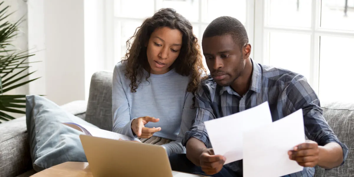 serious african american couple discussing paper documents, sitting together on couch at home, man and woman checking bills, bank account balance, terms of contract, mortgage, loan agreement