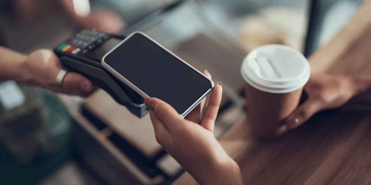 careful progressive lady with manicure holding her smartphone over the credit card payment machine while using contactless payment system