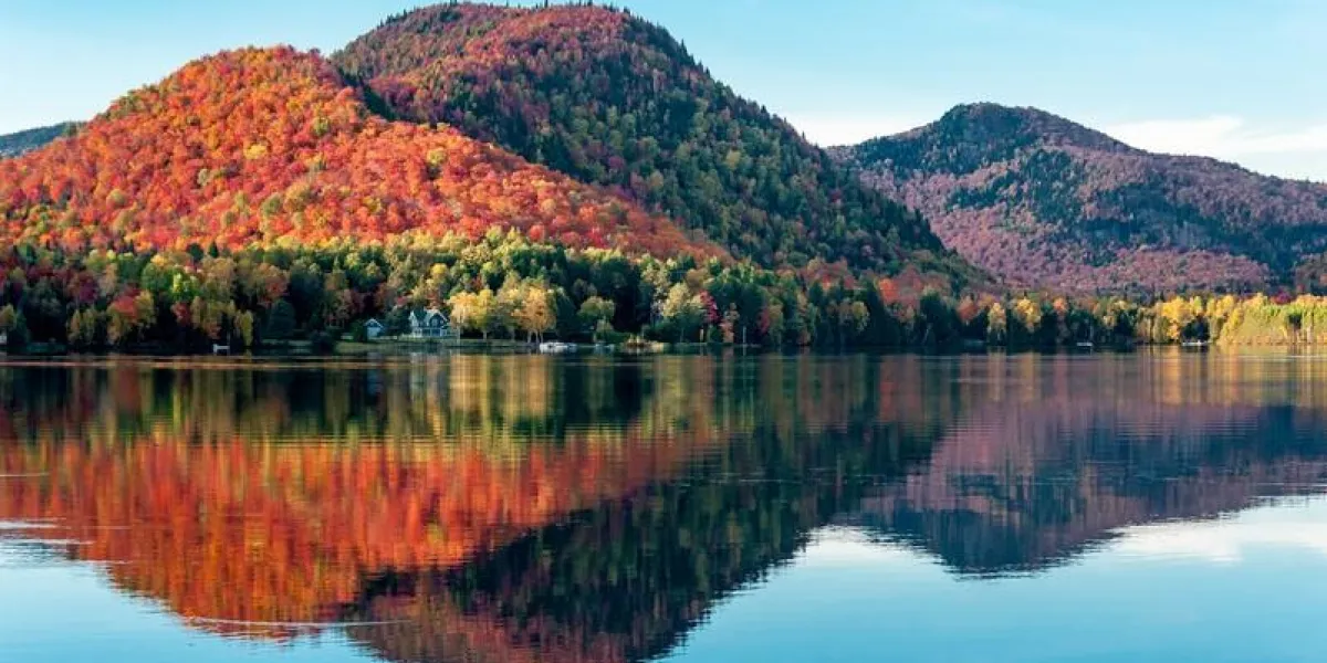 les collines couvertes de forêts d'érables rouges se reflètent dans un lac au québec lors d'une belle soirée d'automne