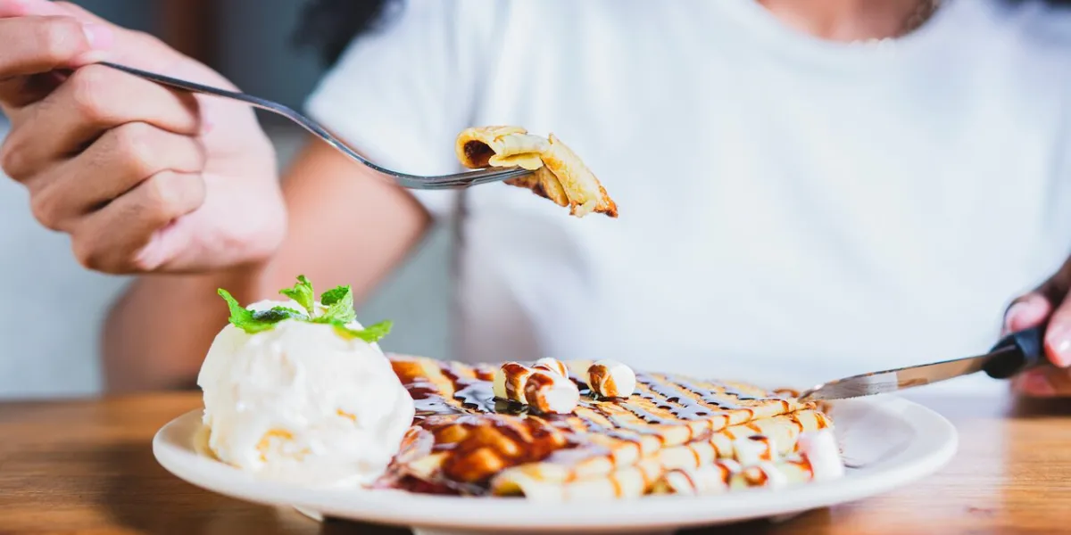 close up of woman eating chocolate crepe and ice cream with fork hands of person with fork cutting chocolate crepe and ice cream