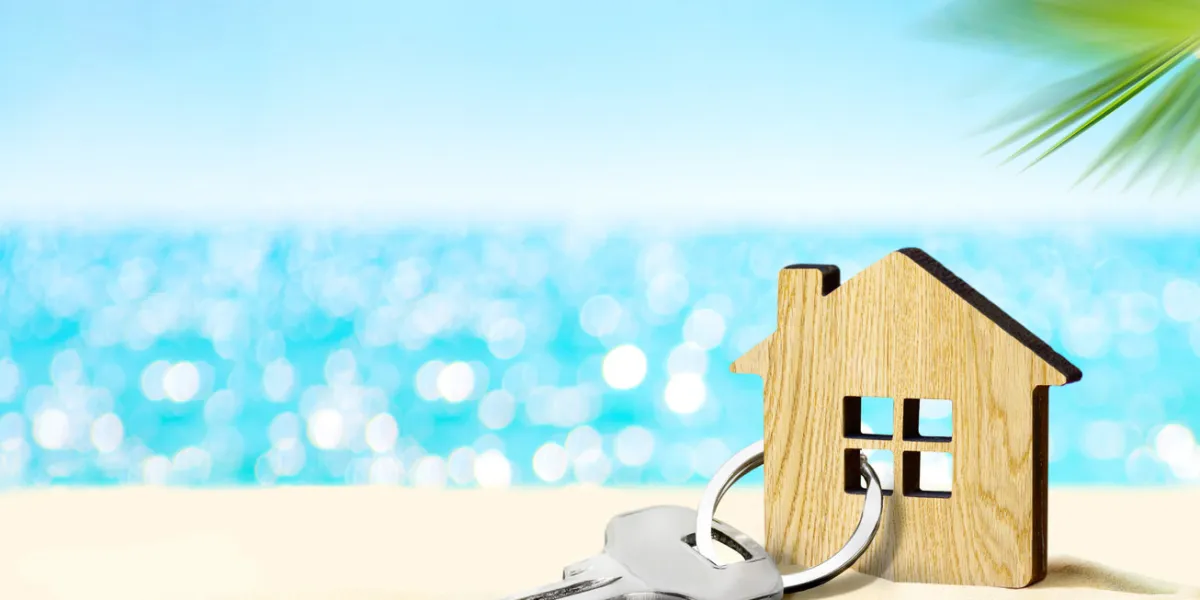 model of house and key on sandy beach with sea and sky on the background