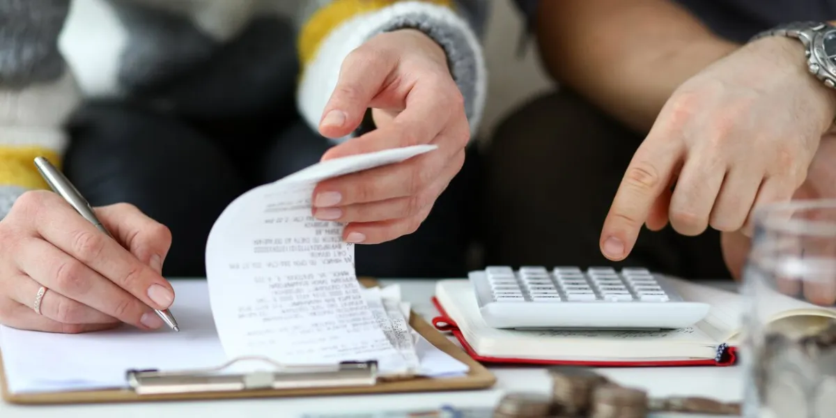 close-up view of man and woman making account of family income writing down and calculating expenses attentive review of finance calculator on desk economy concept