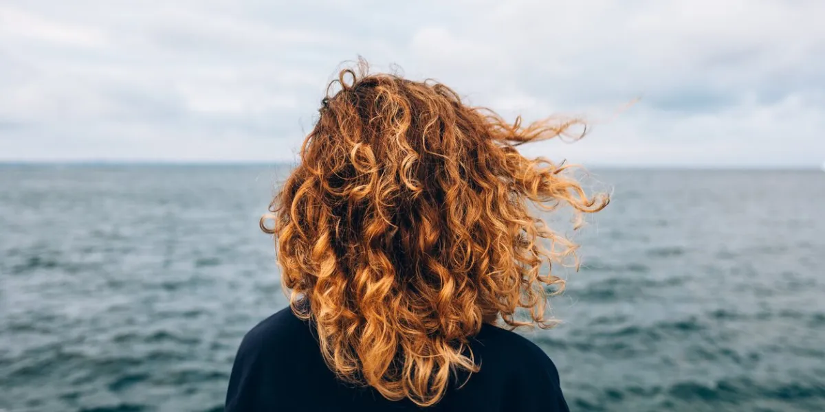 view from the back a woman with curly hair looks at the sea
