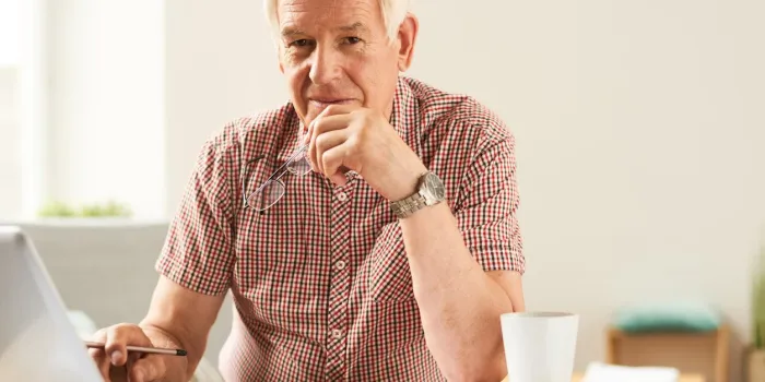 portrait of modern senior man using laptop at home working and looking at camera, smiling