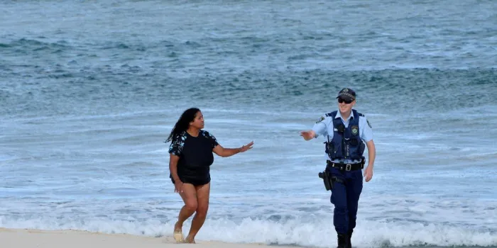 a police officer refrains a woman from swimming on bondi beach in sydney on april 11, 2020 - authorities closed sydney's bondi beach and increased police patrol in an effort to deal with the coronavirus pandemic (photo by saeed khan   afp)