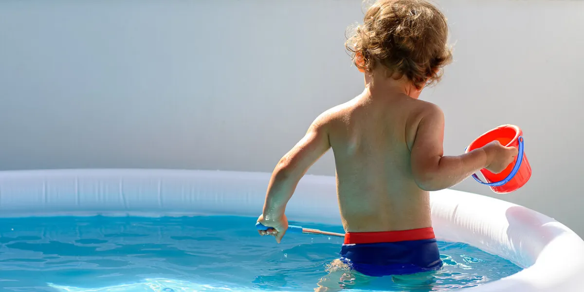 back view of a little boy fishing with a net in the balcony pool water on a hot summer vacation day he is holding a red bucket view of crystal clean water surface, sun shine bright water-pool