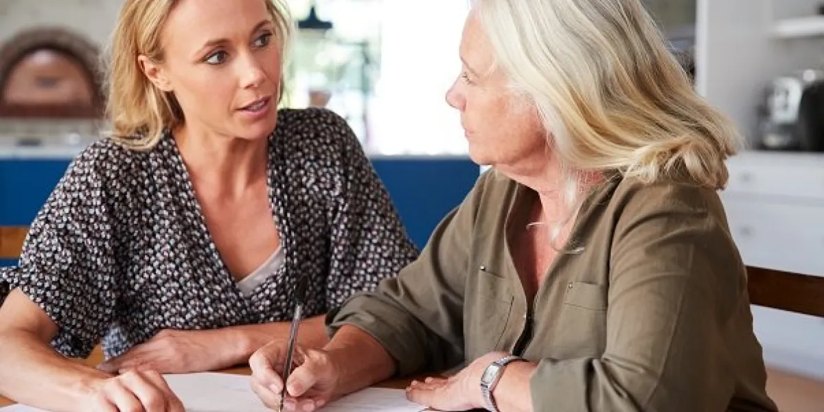female friend helping senior woman to complete last will and testament at home