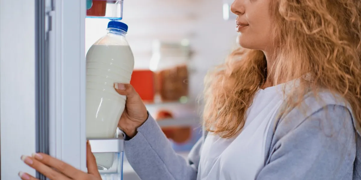 woman standing in front of fridge and taking milk fridge full of groceries