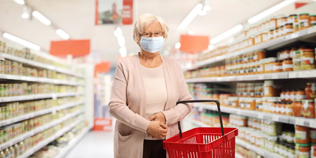 senior female customer with a shopping basket in a supermarket wearing a protective medical mask