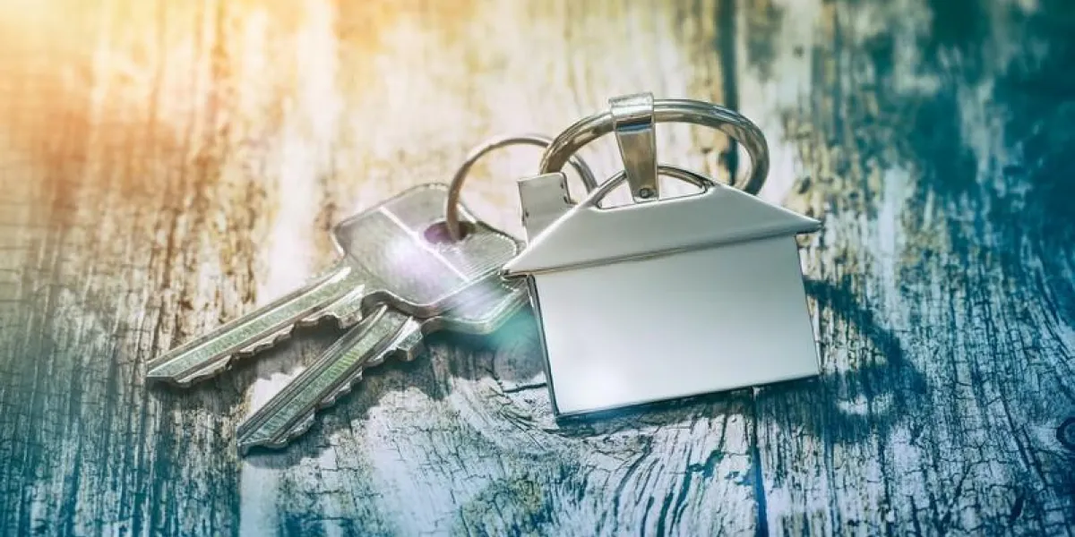 house key on a house shaped keychain on wooden table concept for real estate or renting home