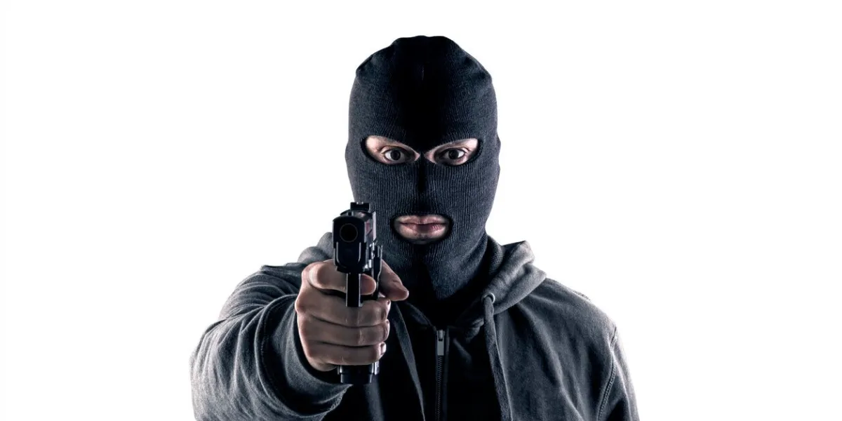 criminal wearing black balaclava and hoodie with a gun isolated on white with clipping path