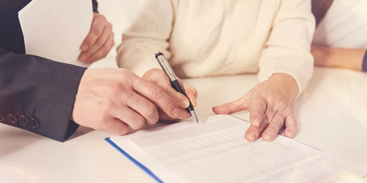 last formalities close up of elderly woman signing papers while meeting with her insurance agent
