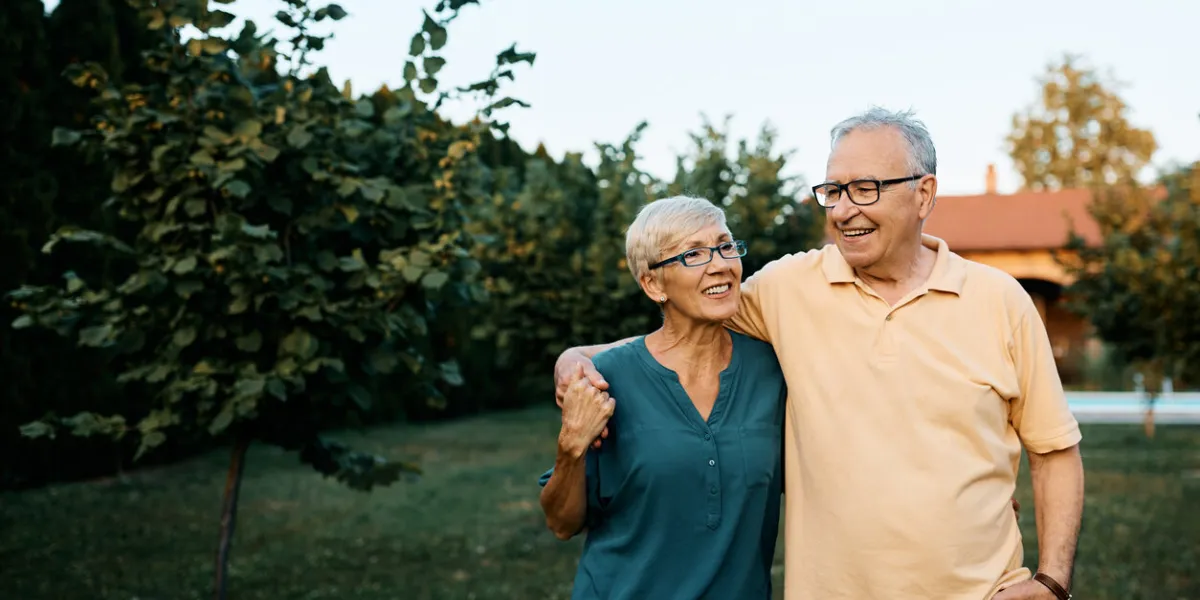 happy senior couple enjoying while walking embraced in their backyard copy space