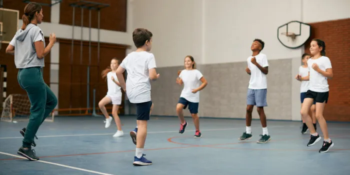 sports teacher and group of kids exercising during physical activity class at school gym