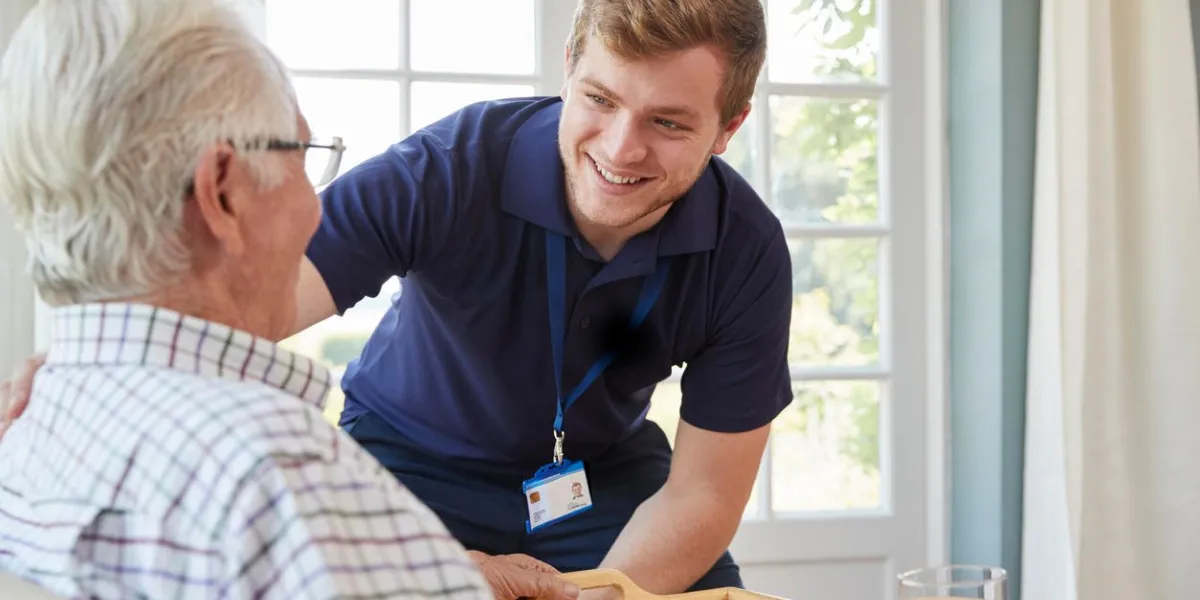 male care worker serving dinner to a senior man at his home