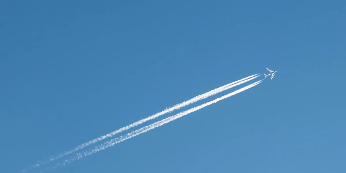 a distant airplane, aeroplane leaving a vapour trail from its four jet engines far up in a deep blue sky