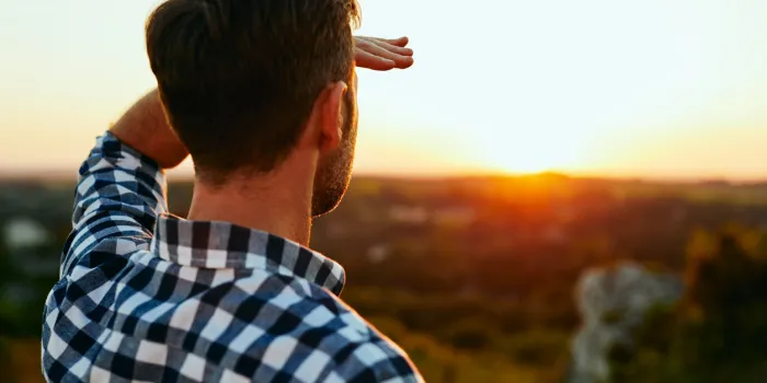 man standing on meadow in mountains and admiring sunset