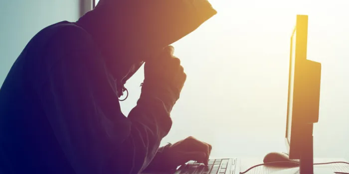 hooded computer hacker hacking network male with black hoodie using computer for identity theft or other criminal online activity