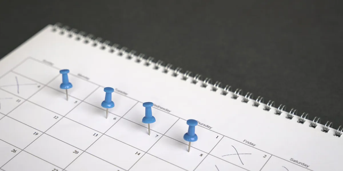 blue pins on four days in a week on a calendar friday, saturday and sunday crossed out four day work week concept