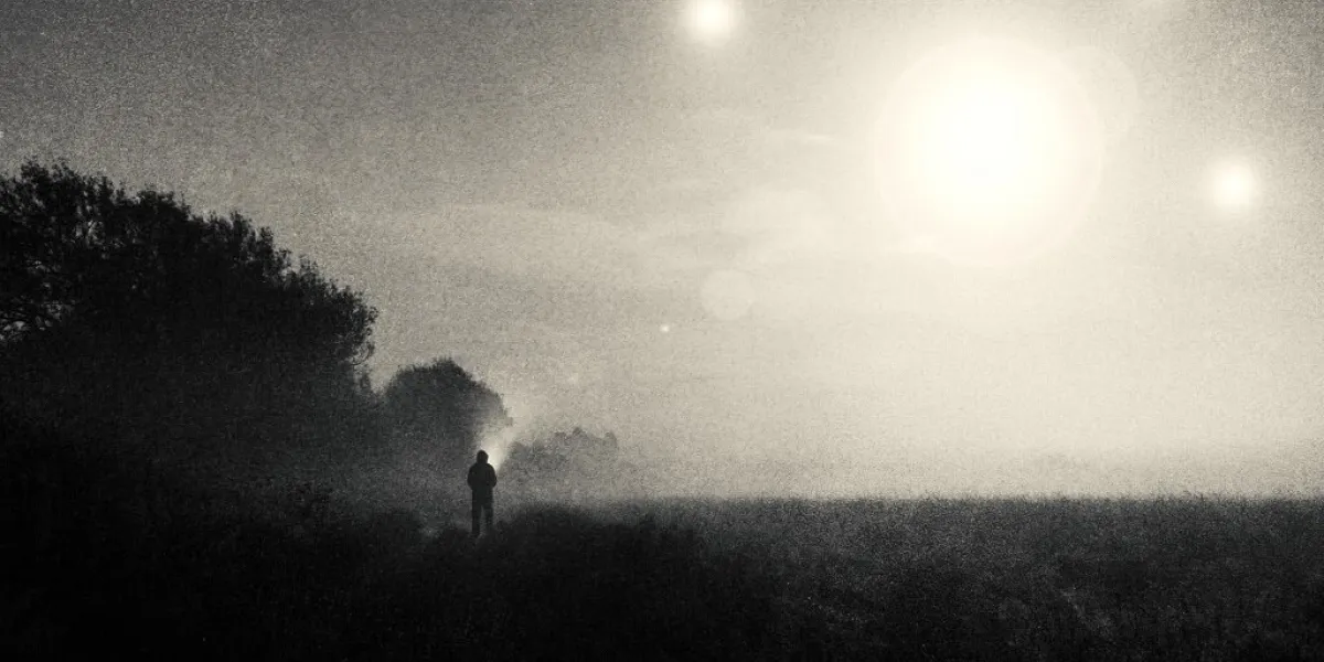 a moody science fiction concept, of a figure standing in a field with ufo lights glowing in the sky on a foggy spooky night with a vintage, grunge edit
