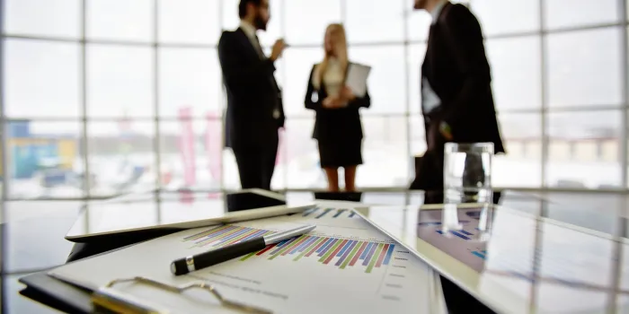 technological devices and financial document at workplace on background of three business partners discussing ideas