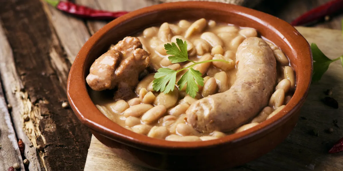 closeup of an earthenware bowl with a cassoulet de castelnaudary, a typical bean stew from occitanie, in france, on a rustic wooden table