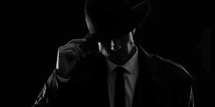 old fashioned detective in hat on dark background, black and white effect