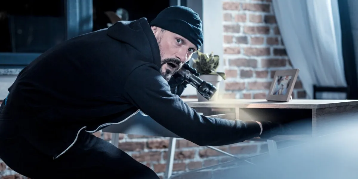 being nervous nervous alarmed bearded burglar wearing black gloves and holding a torch while looking for documents in the table