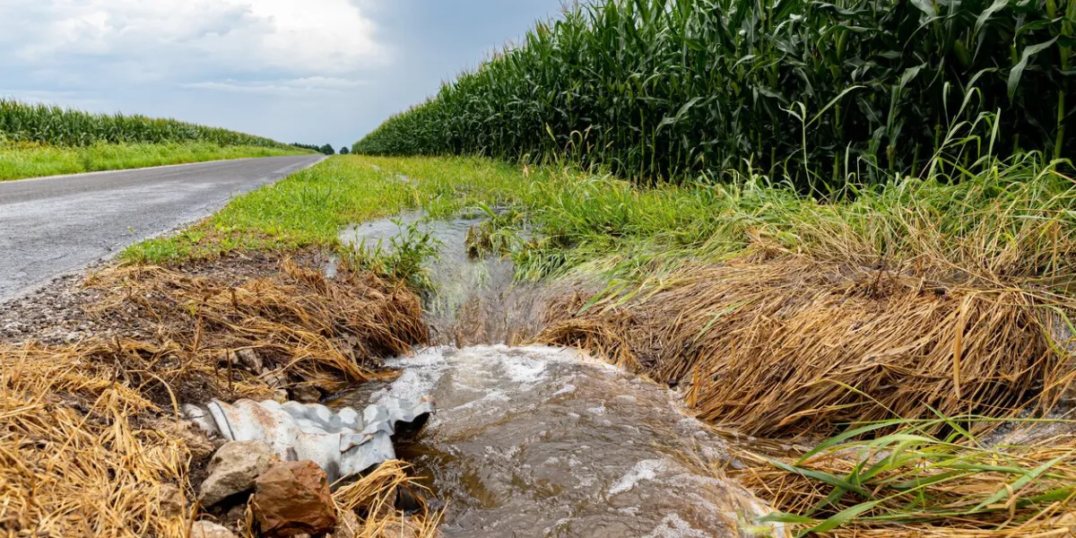 storm water flowing in ditch between road and farm field agriculture runoff pollution, erosion control and weather concept